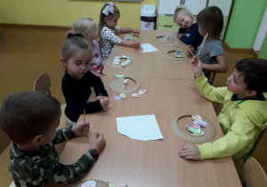 Dzieci przy stolikach wykonują pracę plastyczną owocowy koszyczek.